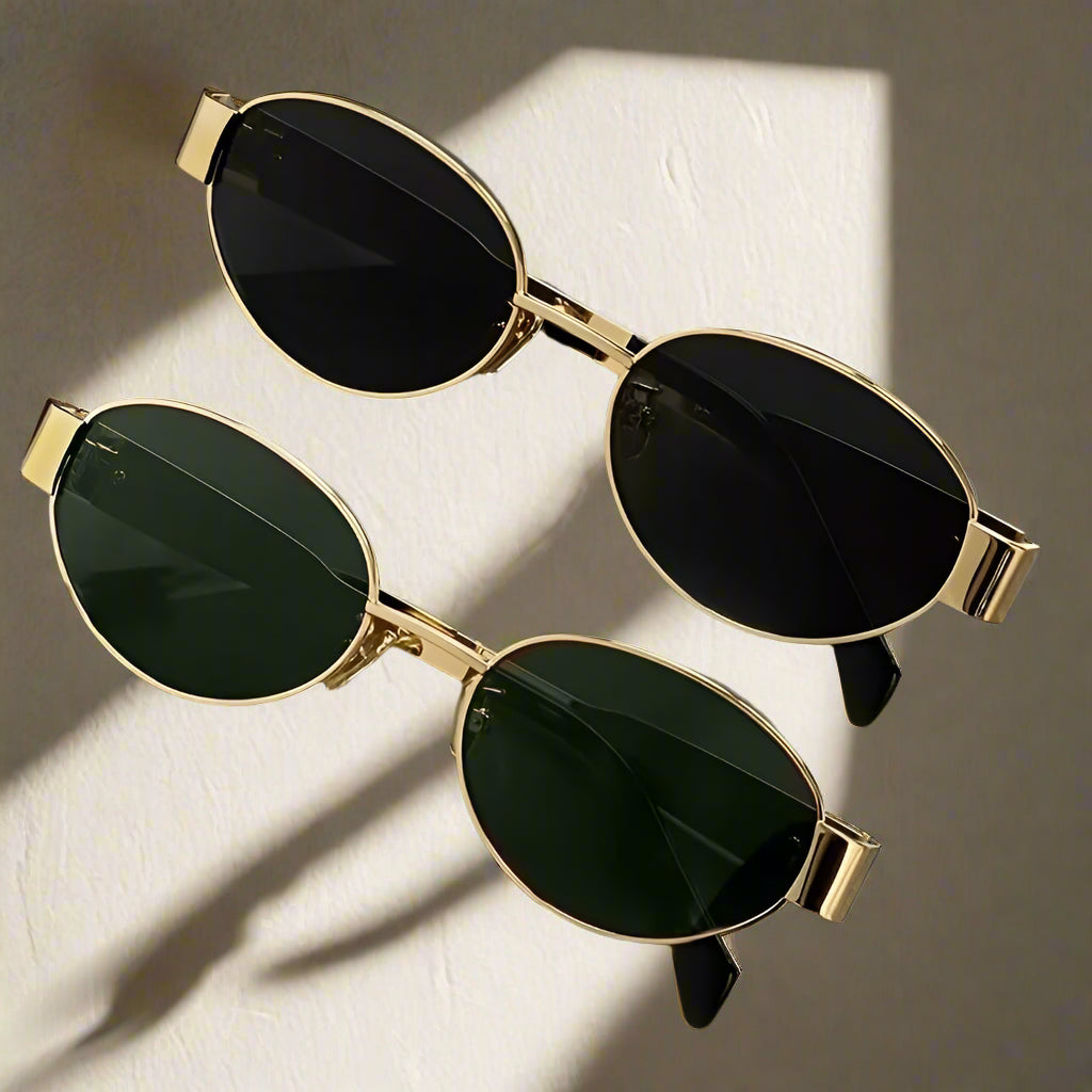 Two pairs of sunglasses with gold frames and dark lenses on a reflective surface.