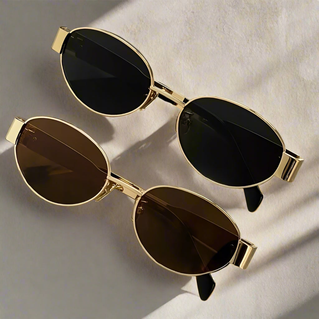 Two pairs of sunglasses with gold frames on a reflective surface.